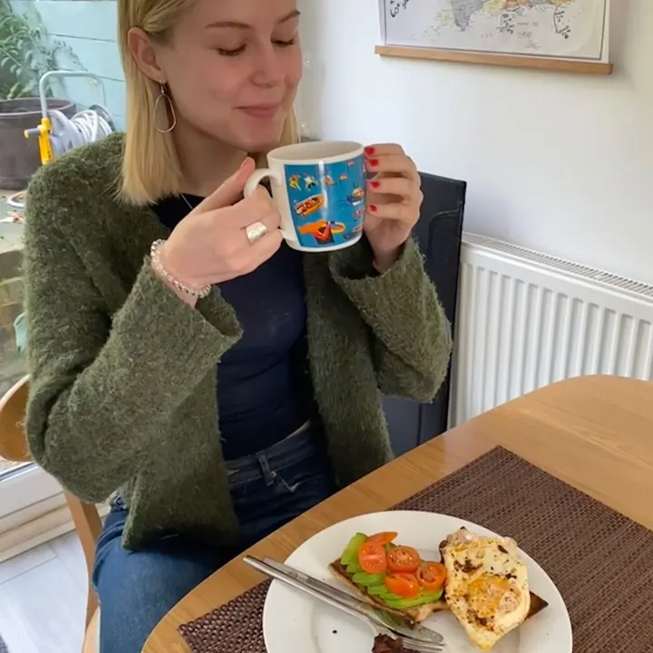 Martha sipping from a mug beside a deconstructed breakfast sandwich