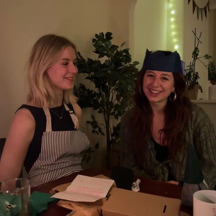 Two friends at the table after Christmas dinner, one in a paper crown