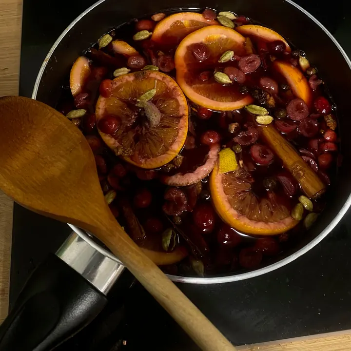 A pan of mulled wine with orange slices and a wooden spoon