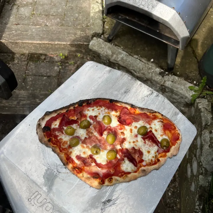 Homemade pizza on a peel beside a pizza oven